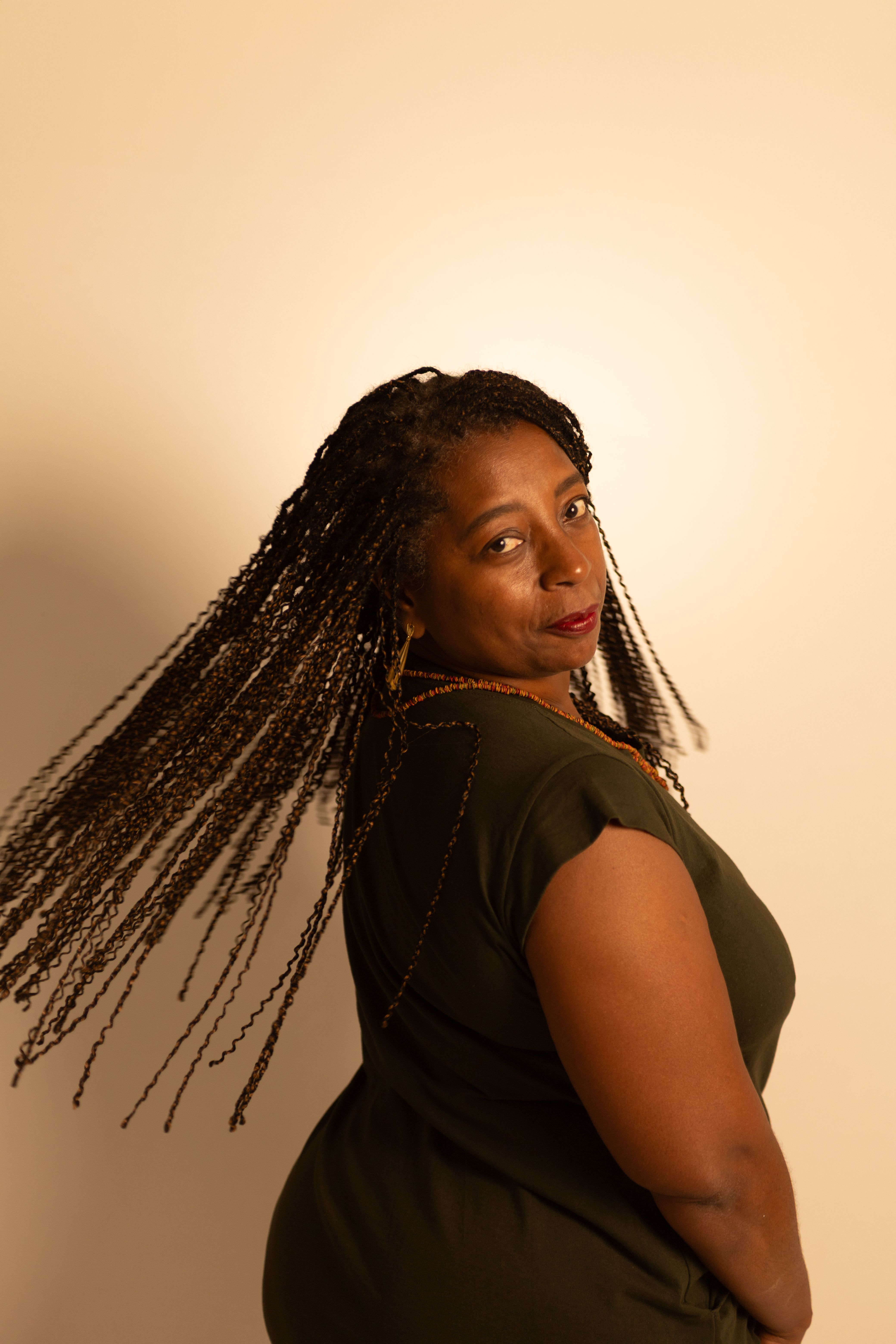 Portrait of an adult woman with braids turning gracefully in a softly lit indoor setting.