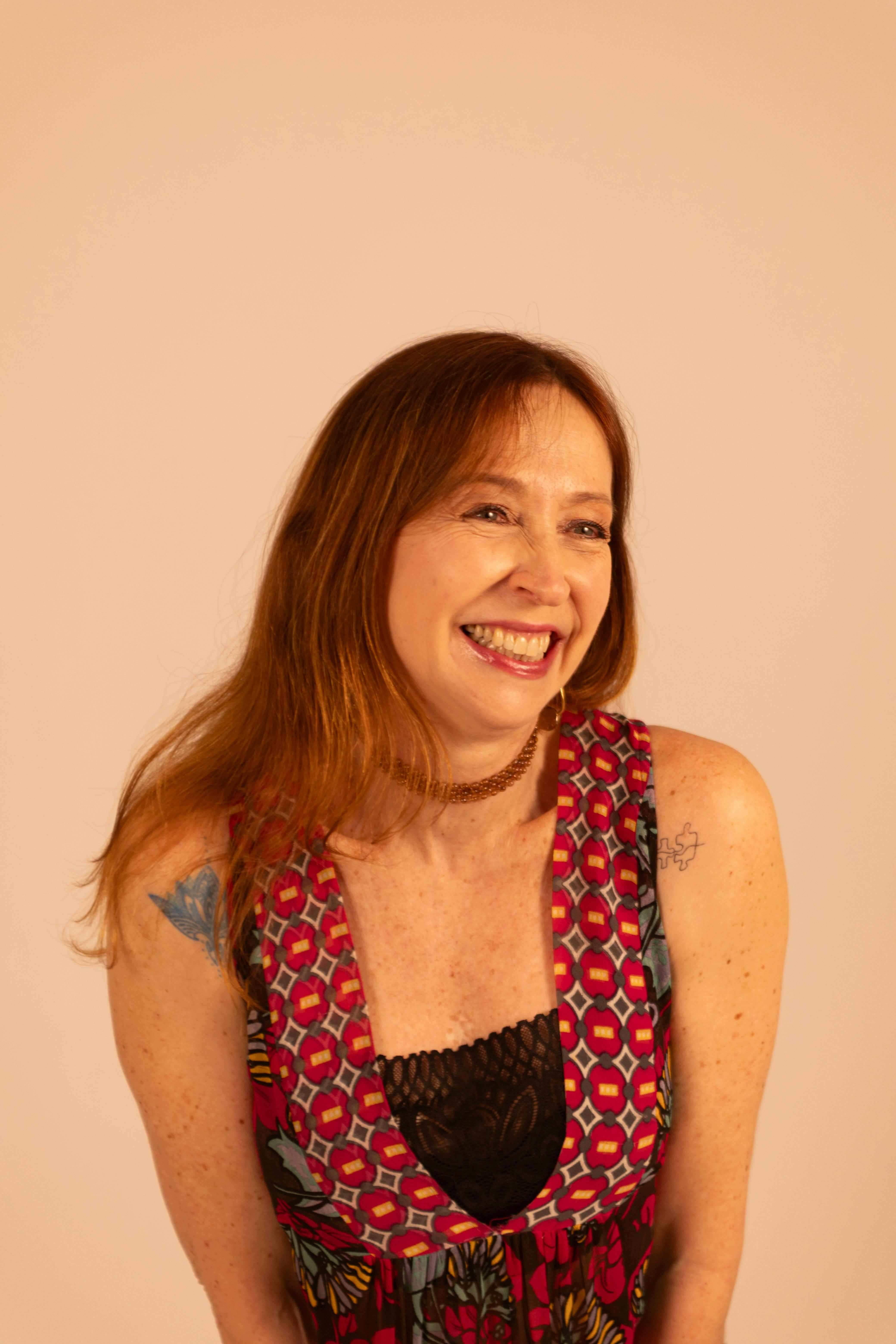 A vibrant portrait of a woman in a patterned dress, captured smiling warmly on a neutral background.