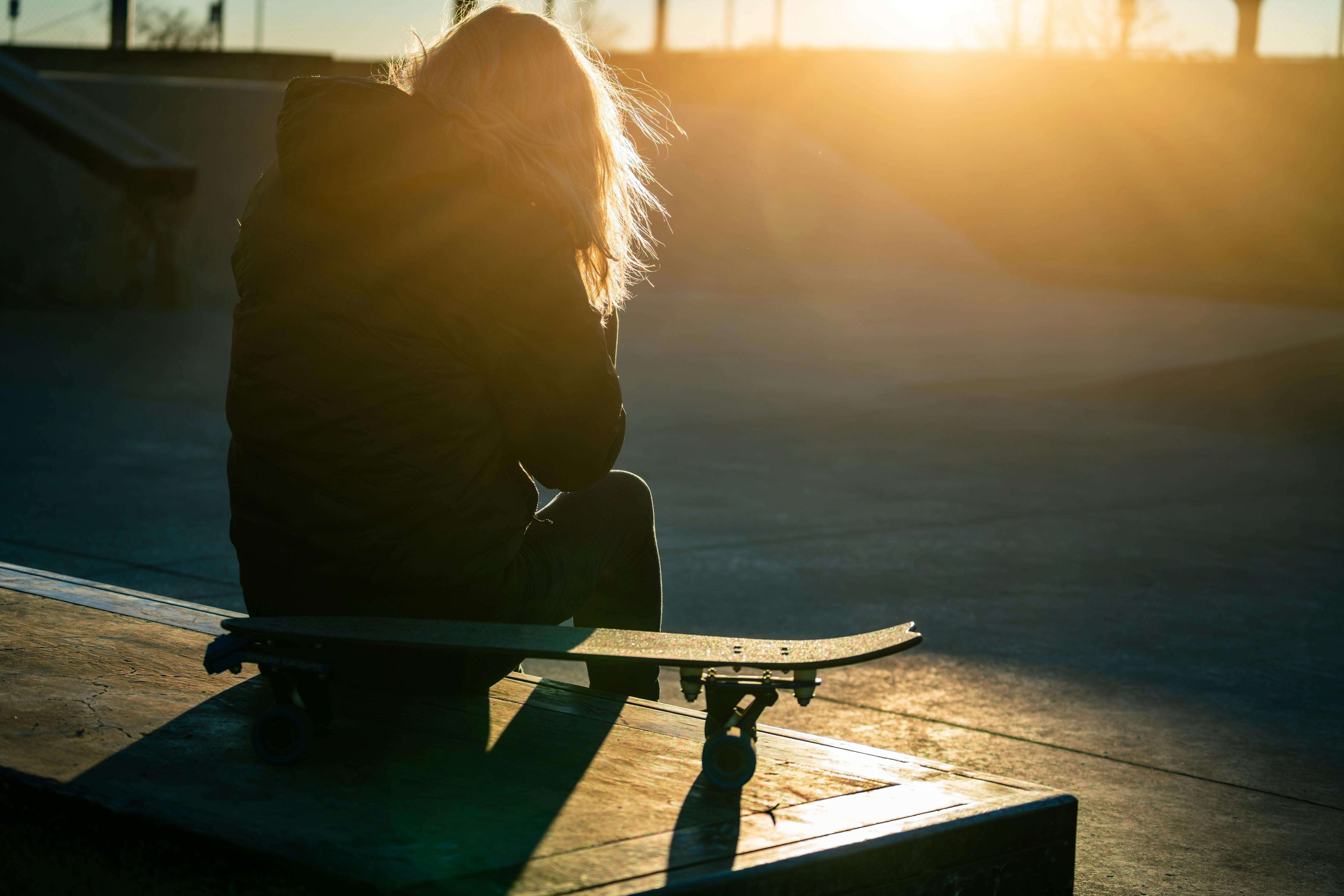 A skater enjoys a tranquil moment at the skatepark during sunrise, backlit by the golden glow.