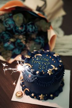 Elegant blue cake with 'Shine Forever 26!' text, adorned with a sparkler for birthday celebration.