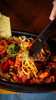 Close-up of a flavorful spaghetti dish with vegetables and shrimp in a black bowl.