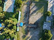 Aerial shot of a large group of people standing in formation on an open field.