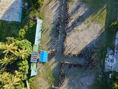 Aerial shot of a large outdoor gathering with people forming a pattern, surrounded by tropical greenery.