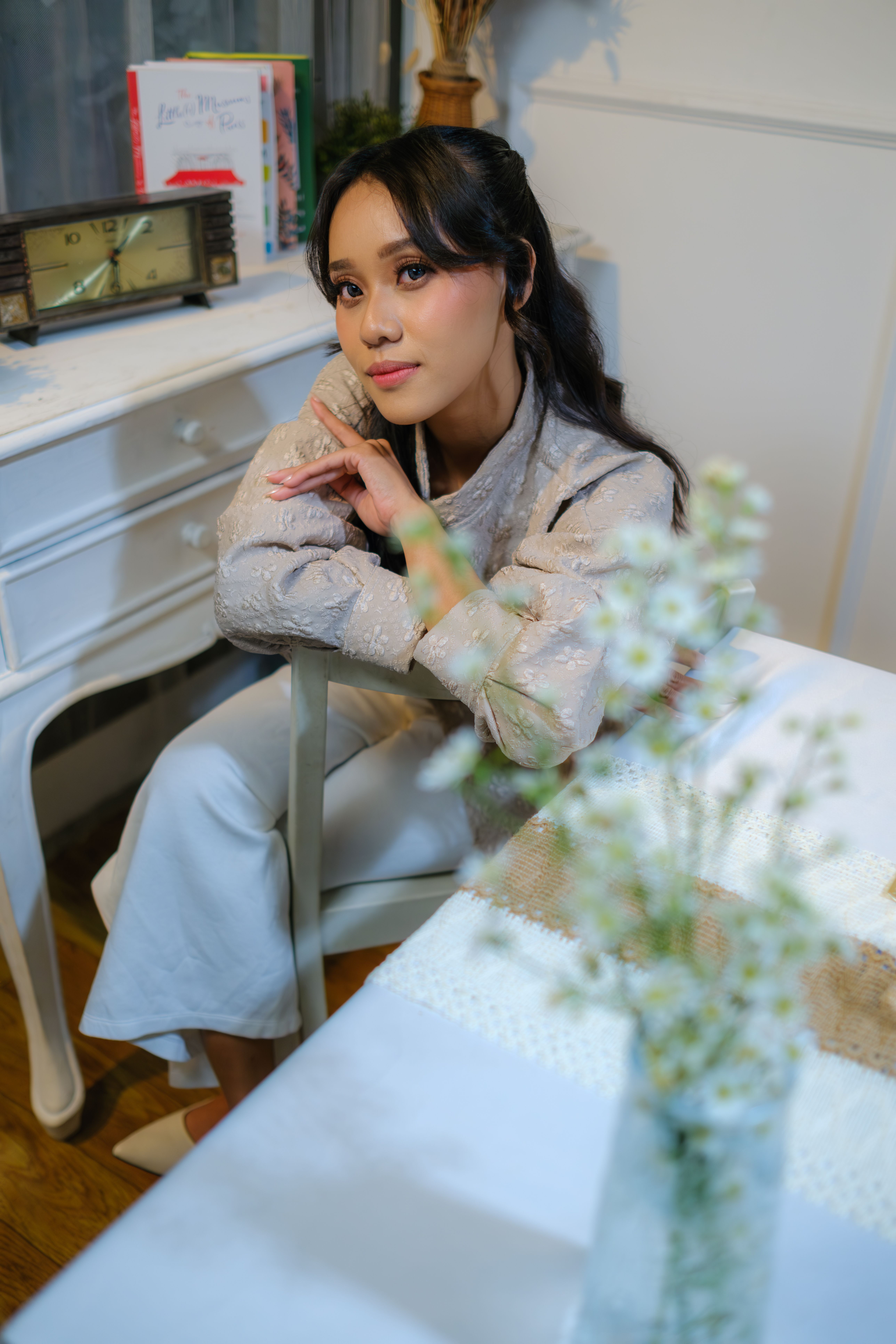 A woman sitting indoors at a table with flowers, exuding a contemplative mood in Jakarta, Indonesia.