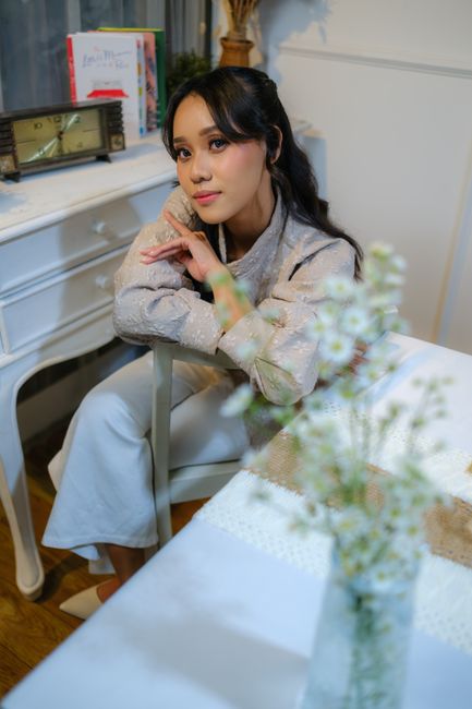 A woman sitting indoors at a table with flowers, exuding a contemplative mood in Jakarta, Indonesia.