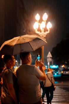A rainy night in Buenos Aires with people capturing streetlife under an umbrella.