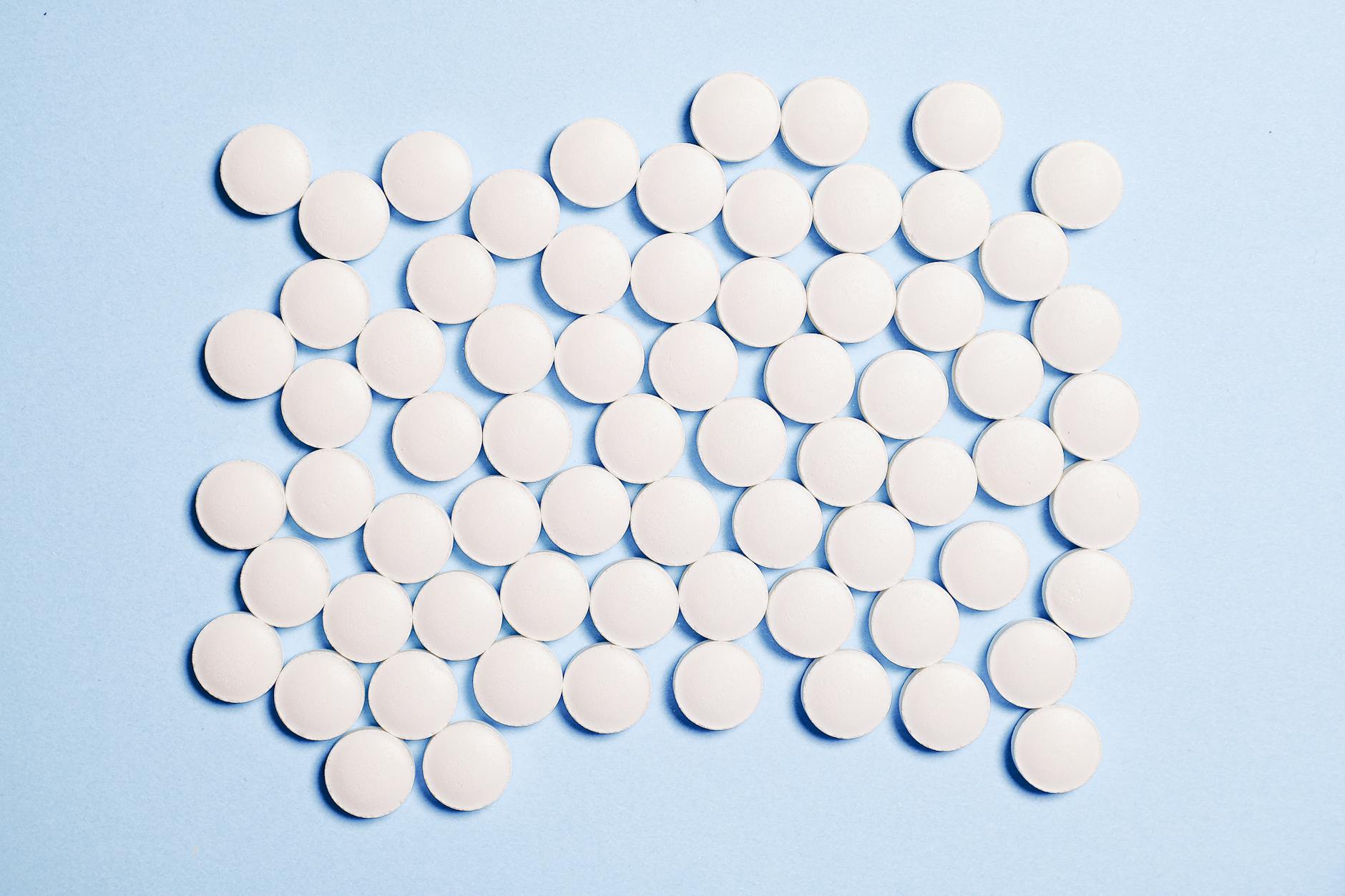 Flat lay of white round pills on a blue surface, ideal for medical-themed content.