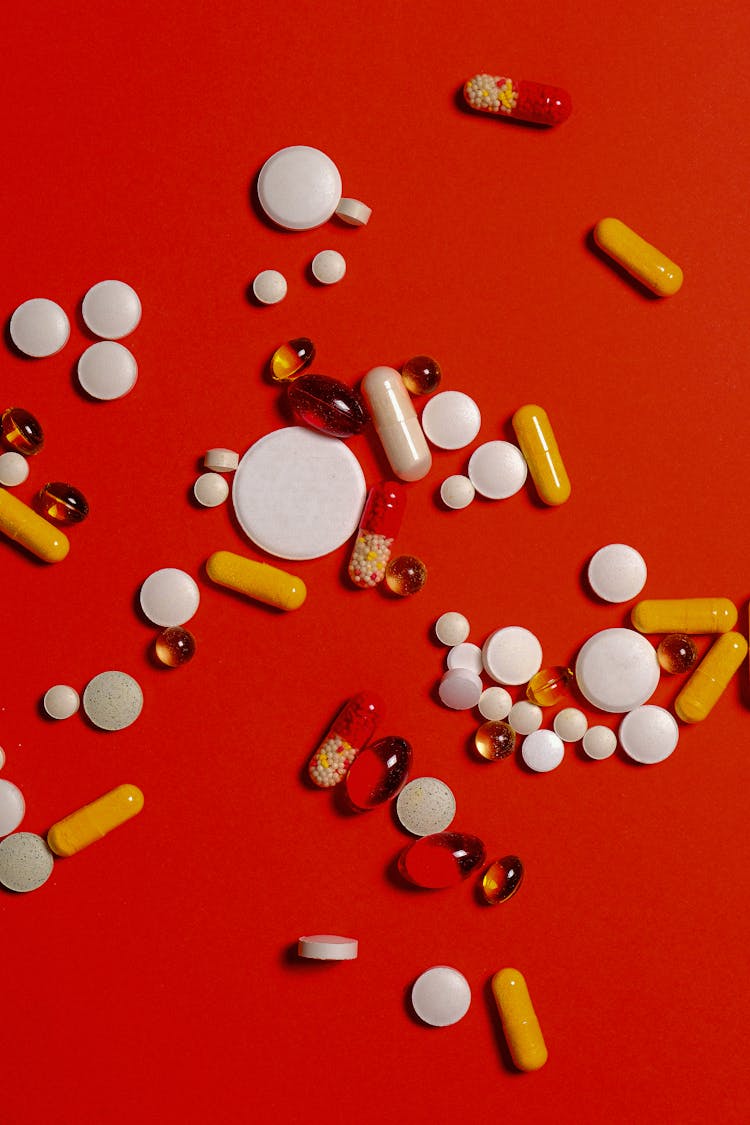 Different Medication Pills And Capsules On Red Background