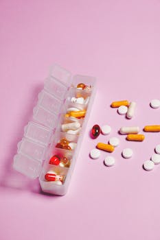 Colorful assortment of pills and capsules in organizer on pink backdrop.