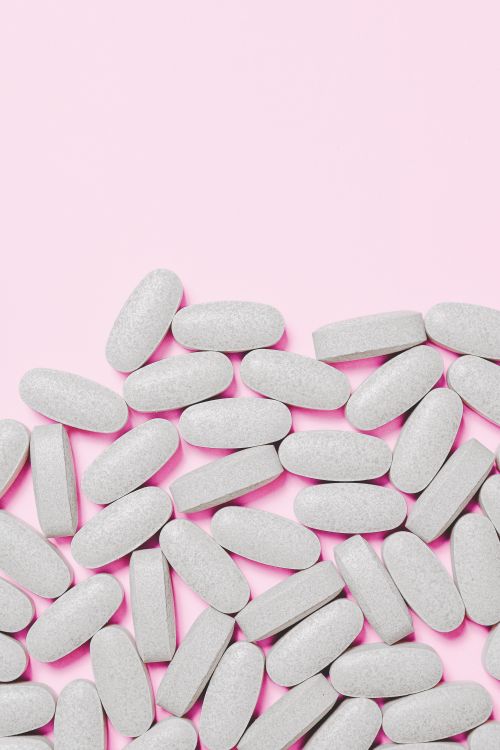 Free Scattered white pills on a soft pink background, representing healthcare and medication. Stock Photo