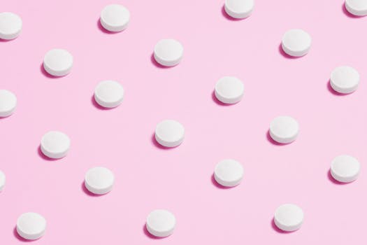 Flat lay of white pills on a pastel pink surface, showcasing a medical theme.