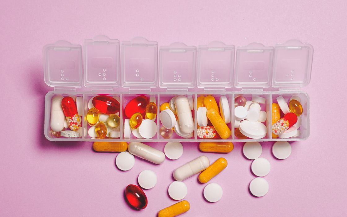 Weekly pill organiser filled with vitamin and mineral supplement capsules on a pink background