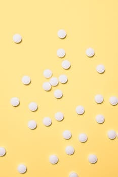 Scattered white pills on a bright yellow surface, ideal for medical themes.