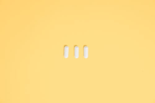 Фото трех белых капсул на желтом фоне