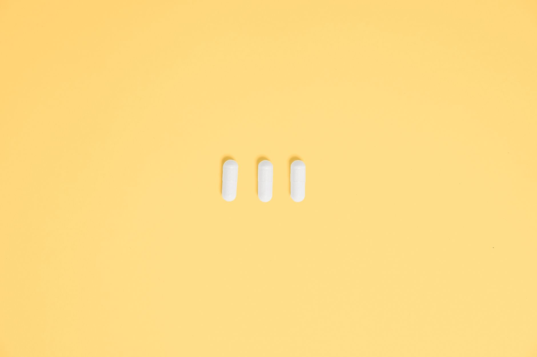 fenbendazole dosing for colon cancer — Three white capsules on a vibrant yellow background, symbolizing healthcare and medication.