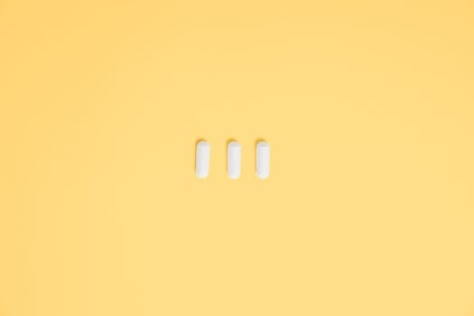三个白色胶囊置于充满活力的黄色背景上，象征着医疗保健和药物