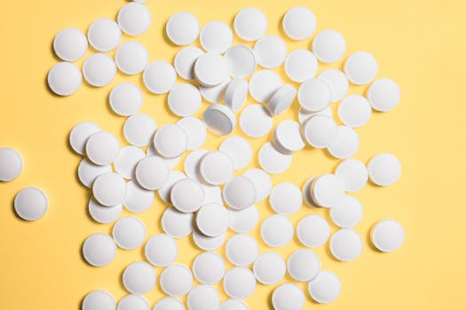Scattered white pills on a vibrant yellow background, symbolizing healthcare and medicine.