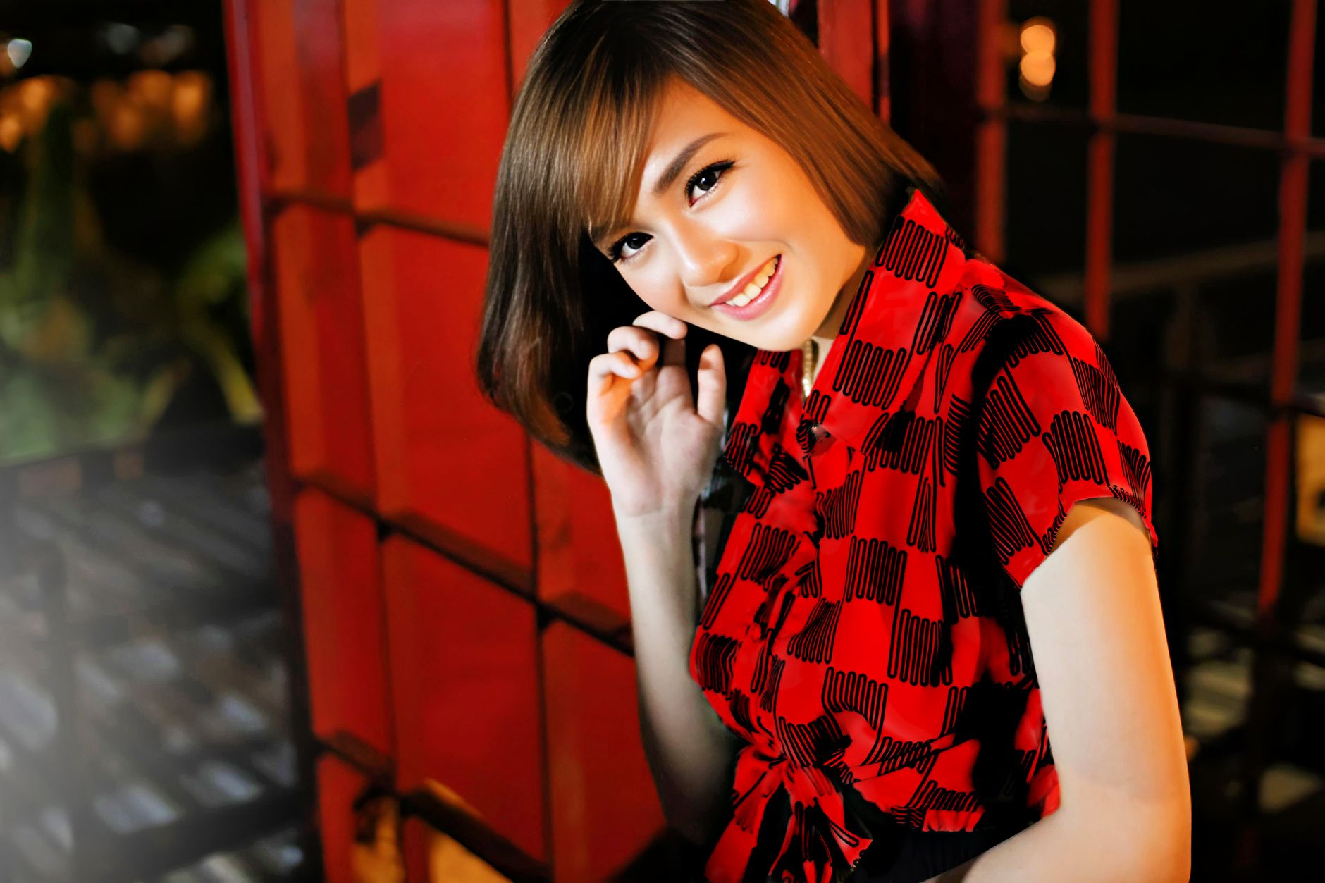 A vibrant portrait of a woman smiling in a red dress, set against an urban backdrop at night.