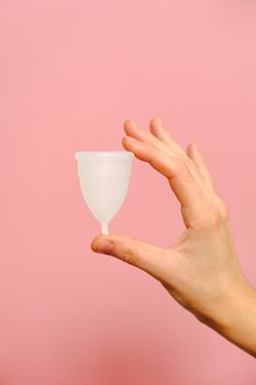 在粉红色背景前，手持可重复使用的月经杯，倡导环保女性卫生