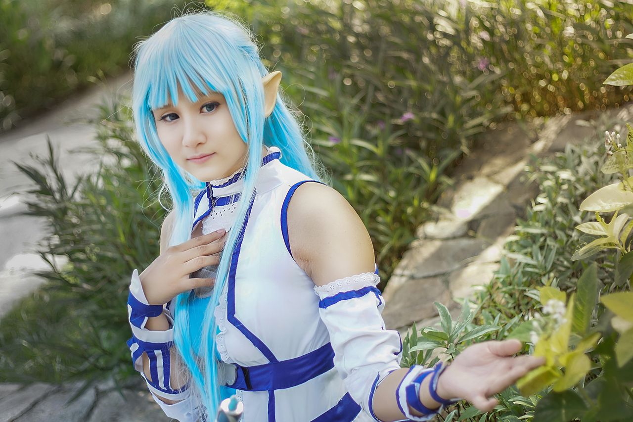 a whimsical cosplay character with blue hair poses in a lush surabaya