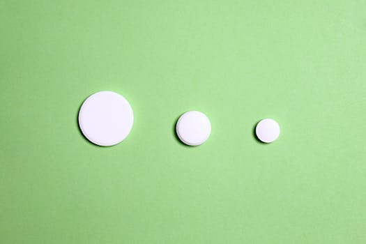 Three varying sizes of white tablets on a green surface, symbolizing medicine dosage.