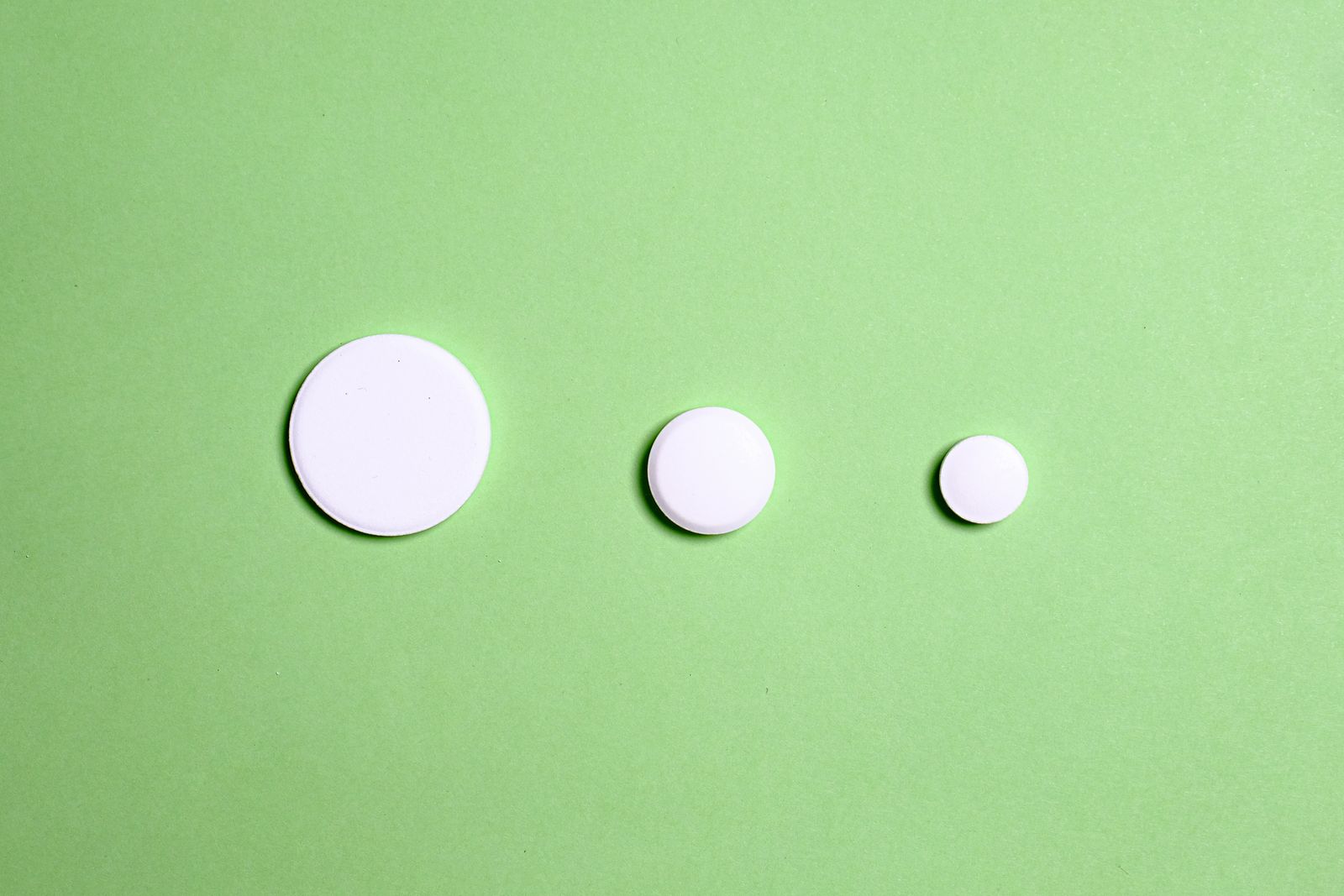 Three white tablets of different sizes lined up on a flat green surface