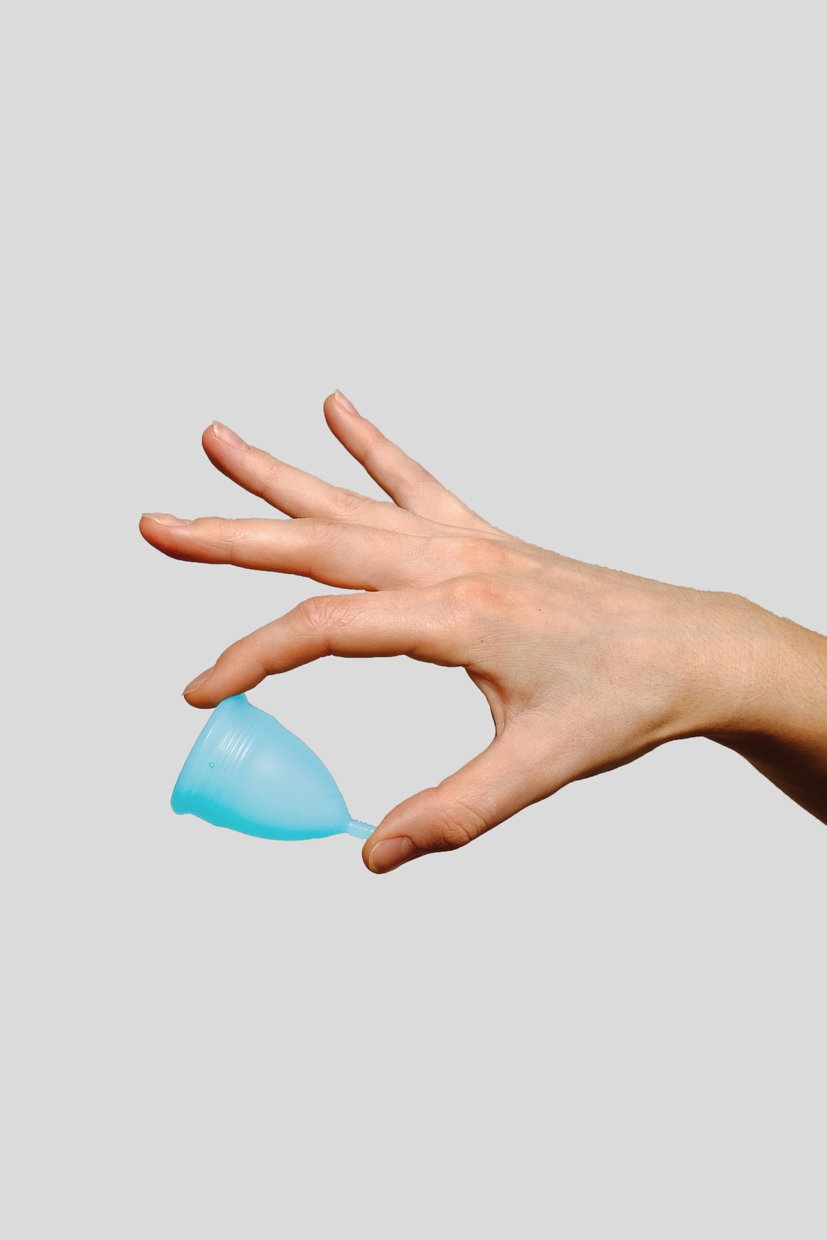 A hand holding a soft blue silicone menstrual cup against a plain grey background