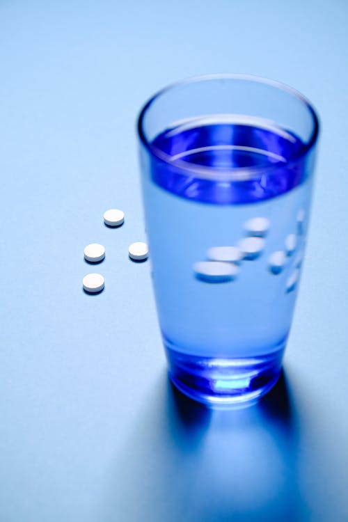 Gelas Minum Biru Dengan Air Dan Pil Obat Putih