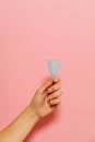 一只手拿着可重复使用的月经杯，背景是柔和的粉色