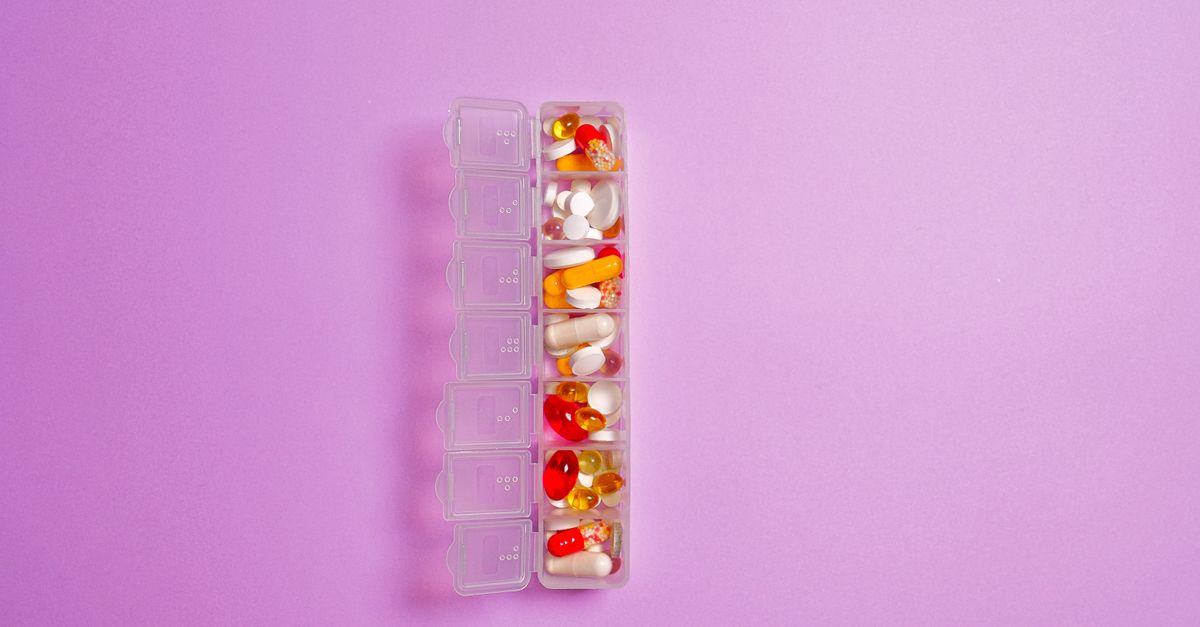 Close-up of assorted pills in a weekly organizer against a violet background.