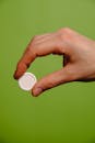 特写镜头中，一只手拿着一颗白色药丸，绿色背景突出了药物