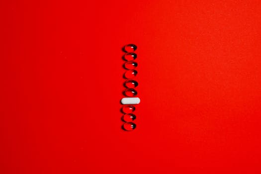 Minimalist setup of a white capsule surrounded by black gel pills on a vibrant red surface.