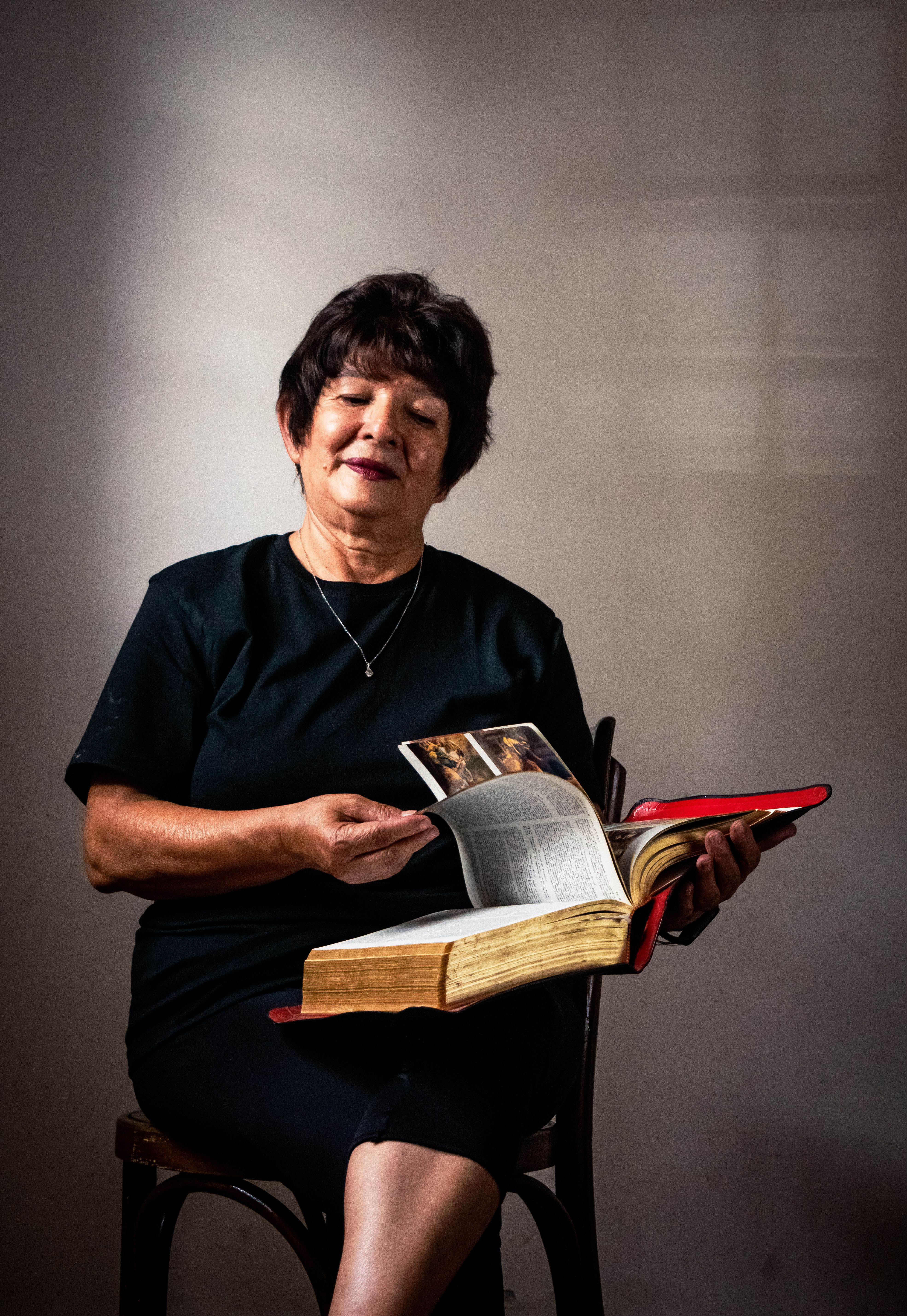 A senior woman sitting indoors while reading a large book, evoking wisdom and concentration.