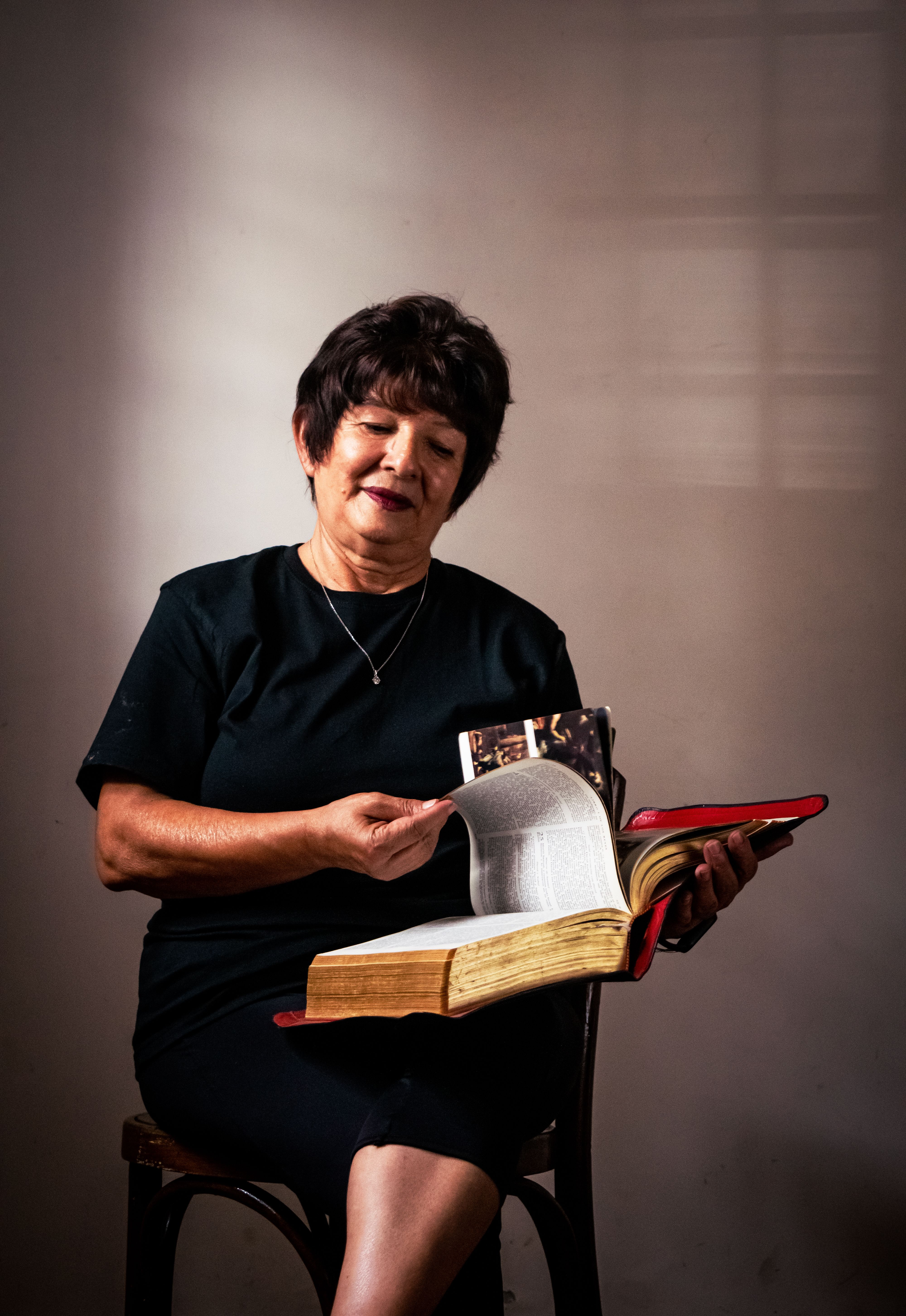 Senior woman reading a large book indoors with focused expression, depicting relaxation and learning.