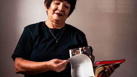 Senior woman reading a large book indoors with focused expression, depicting relaxation and learning.