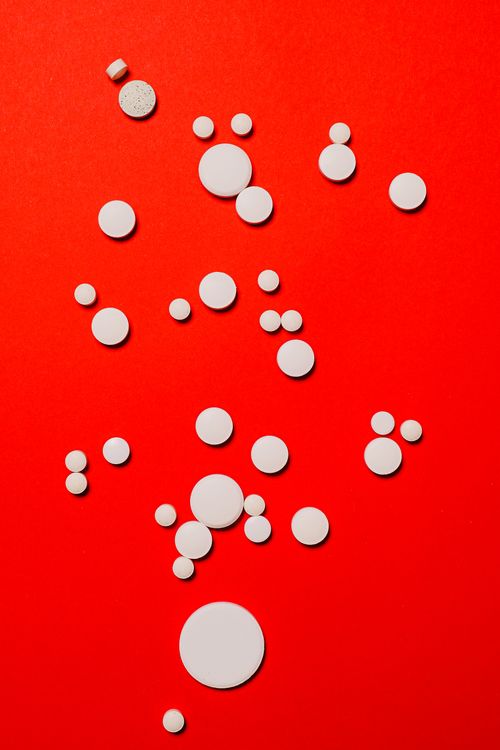 Free Flat lay of white pills scattered on a vibrant red background, ideal for medical and pharmaceutical themes. Stock Photo