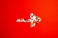 在鲜艳的红色背景上，五彩药丸排列成箭头的艺术造型