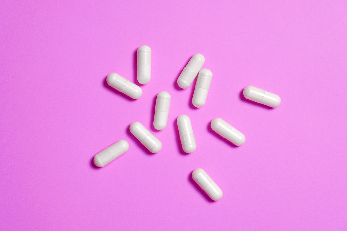 White supplement capsules scattered on a bright pink background