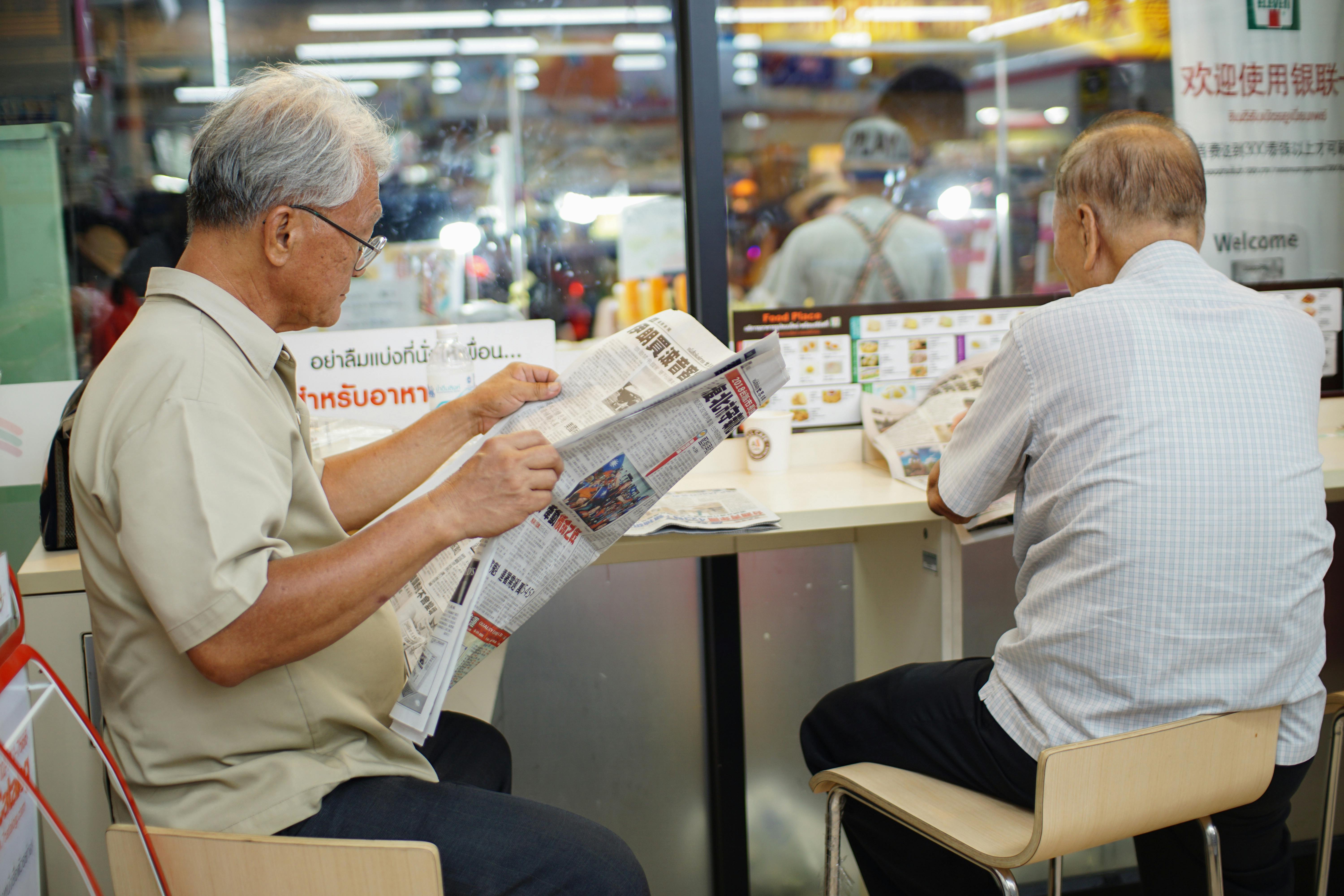 Two elderly men read newspapers inside a cafe in Bangkok, capturing a moment of daily life.