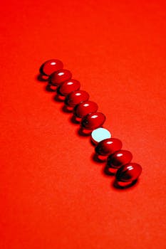 A row of red pills with a single white pill on an orange background.