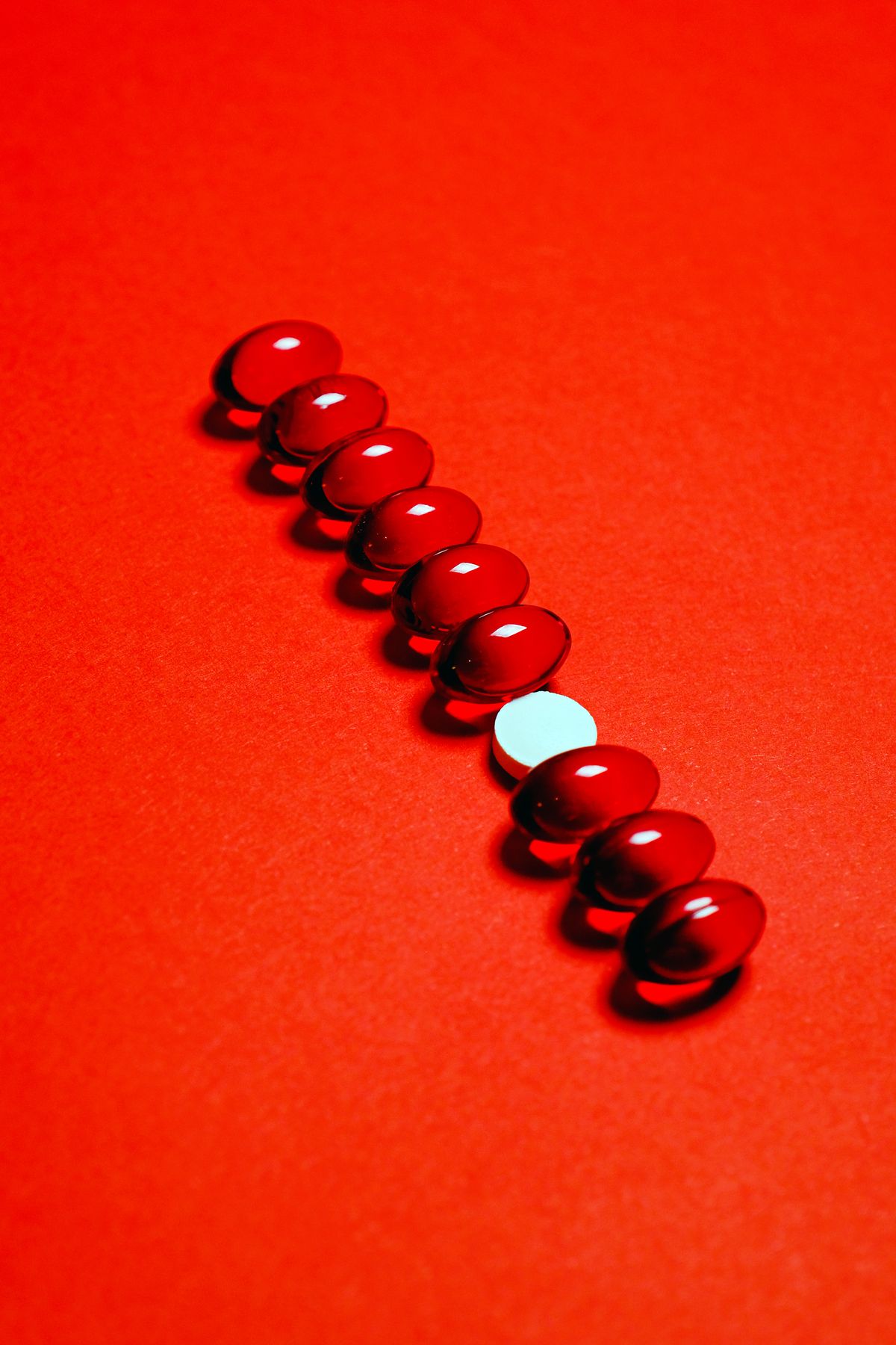 A single white tablet breaking a row of red capsules