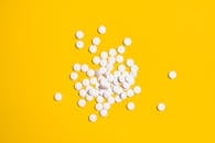 一组白色药丸散落在亮黄色背景上，象征着医疗保健和医学