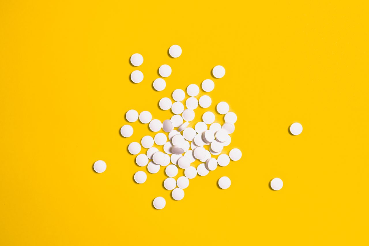 a group of white pills scattered on a bright yellow background symboli