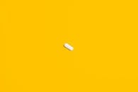 一颗白色药丸置于亮黄色背景之上，凸显了其简洁与重点