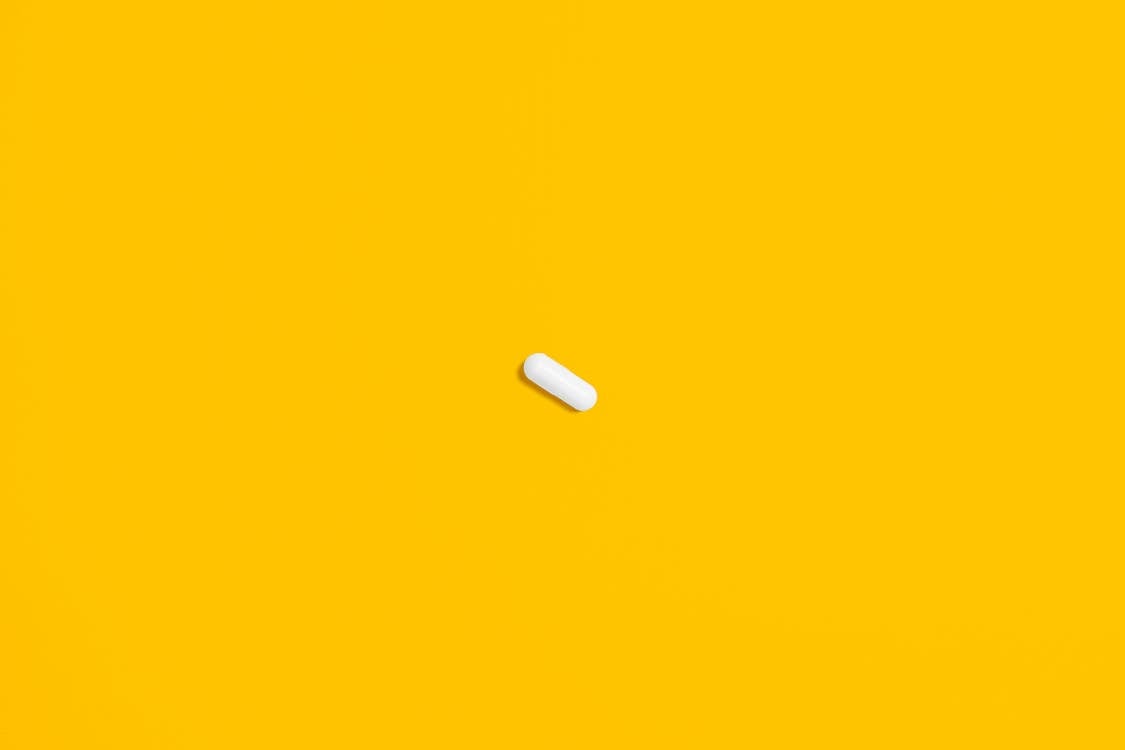 Free White Pill on Yellow Surface Stock Photo