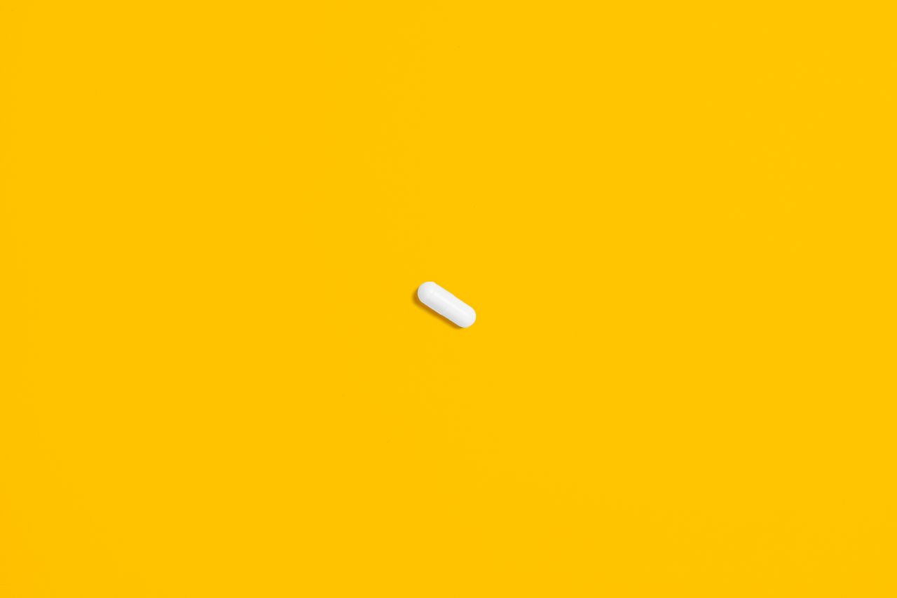 a single white pill lies against a bright yellow background highlighti