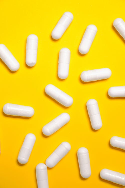Белые капсулы лекарства на желтой поверхности