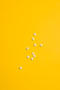 白色药丸散布在鲜艳的黄色背景上，非常适合制药主题