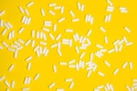 白色药丸散布在鲜艳的黄色背景上，突出了医疗保健和药物主题