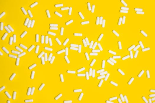 Scattered white pills on a vibrant yellow background, highlighting healthcare and medication themes.